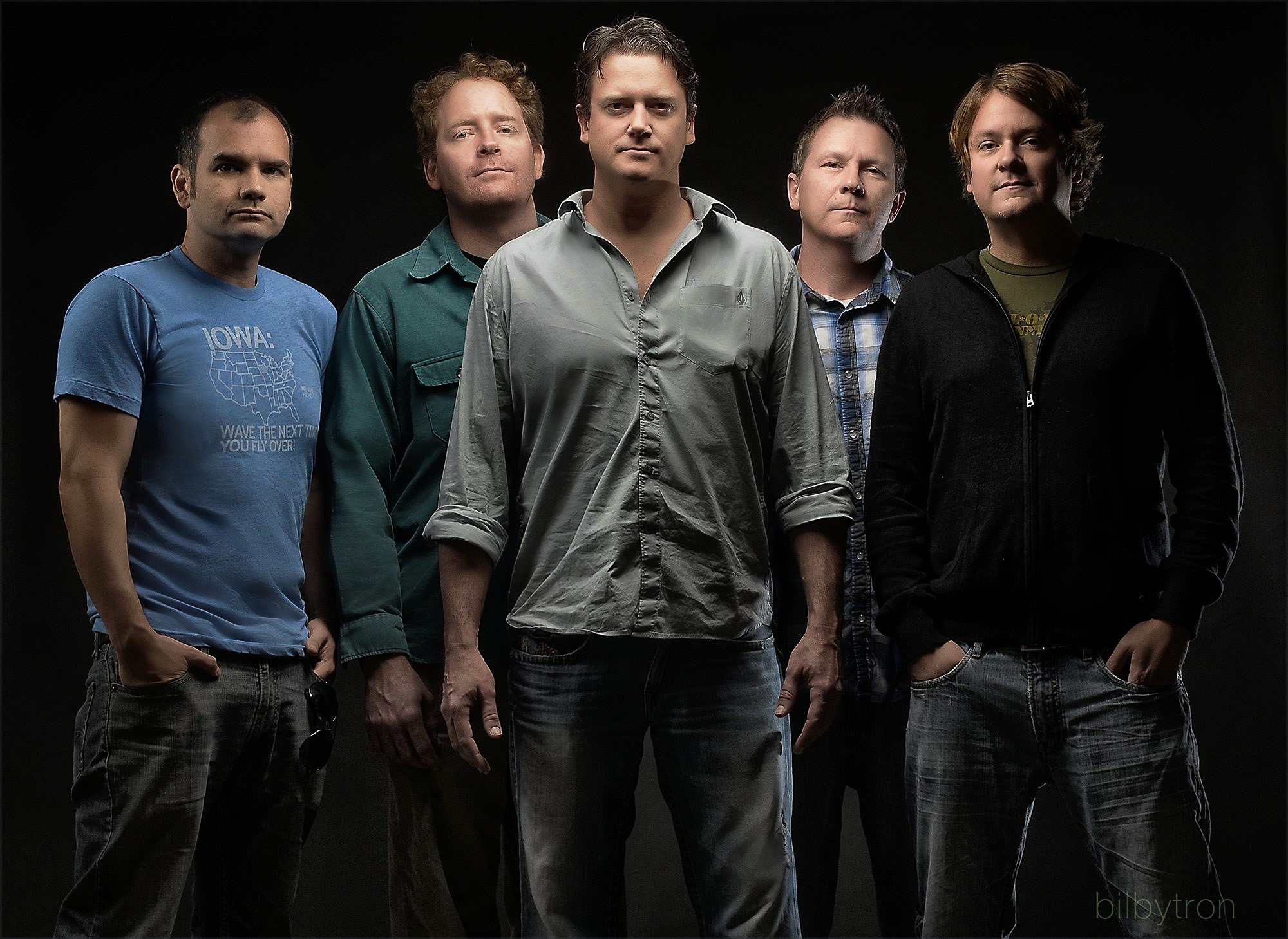 Five band members photographed together against a black background